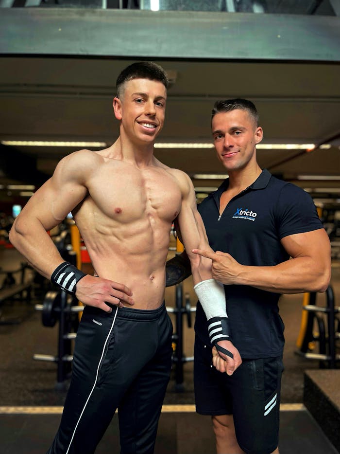 Two muscular men smiling and posing in a gym, showcasing bodybuilding physique and camaraderie.